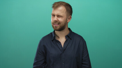 Obraz premium Man with beard and visible chest smiling with slight head tilt wearing a navy shirt in teal studio; friendly.