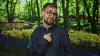 Fototapeta premium Man with hand on chest and glasses standing among tulip beds in forest park, green outdoors; contemplation.