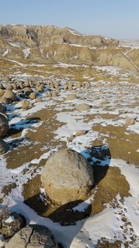 Grand aerial drone shot of a giant spherical stone concretion in the Torysh Valley during winter. This massive round boulder is a unique remnant of the ancient Tethys Ocean floor. The snow-covered des