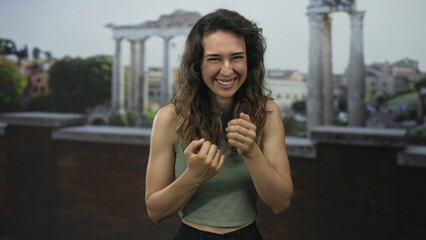 Fototapeta premium Young hispanic smiling woman points finger to historic building on street framed by ancient columns; joy.