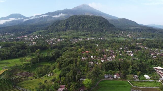 Aerial view of Mount Welirang with terraced rice fields, rural village settlement, and green valley landscape in East Java, Indonesia