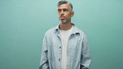 Obraz premium Man with grey hair and face visible, eyes closed and lips pursed while looking sideways in a studio teal backdrop; calm contemplation.
