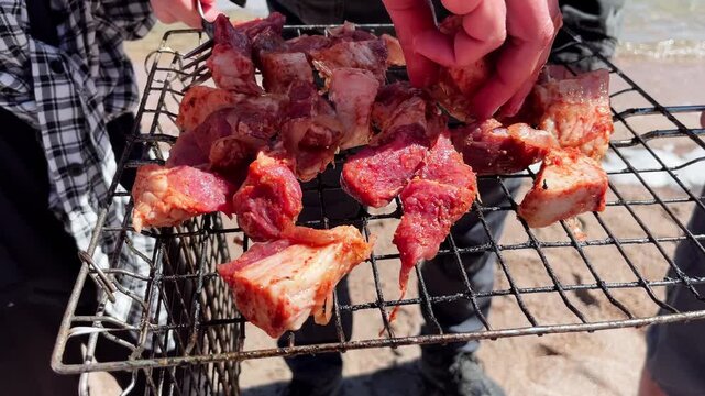 People arranging raw marinated meat on a grill rack at the beach