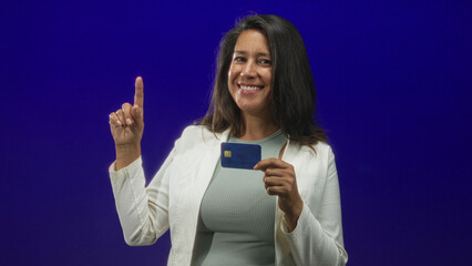 Fototapeta premium Woman holding creditcard and points index finger while smiling in studio; confidence financial empowerment.