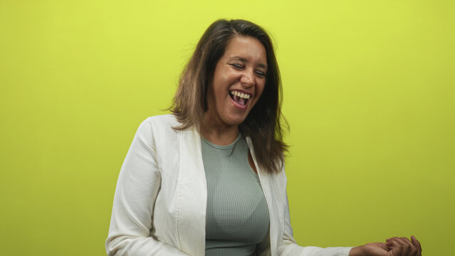 Woman middle age brunette headbanging and miming air guitar with clenched hand and laughing against lime green studio wall; joy.