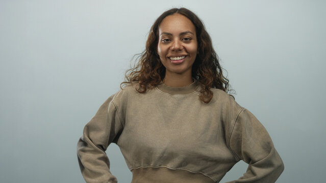 Young african american woman smiling with hands on hips wearing cropped sweatshirt in pale blue studio; confidence casual warmth.