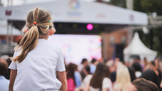 Little girl watching outdoor summer concert from audience at music festival