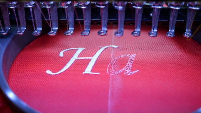 Machine embroidery on red fabric with white thread. A professional embroidery machine sews text. Close up 4k video
