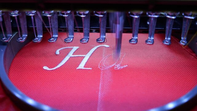 Machine embroidery on red fabric with white thread. A professional embroidery machine sews text. Close up 4k video slow motion