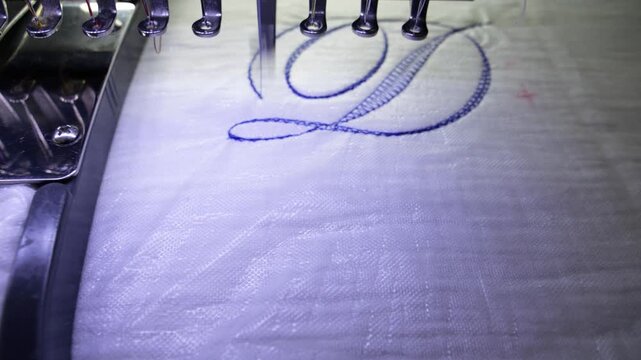 Machine embroidery of the letter "D" on white fabric with blue thread. Selective focus close-up
