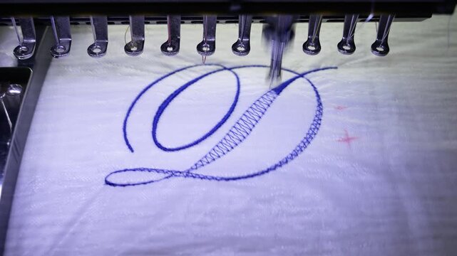 Machine embroidery of the letter "D" on white fabric with blue thread. Selective focus close-up
