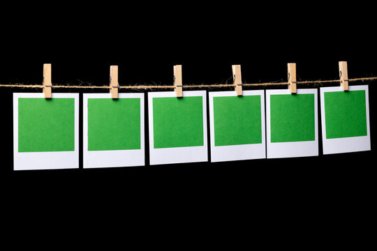 Six green rectangular sheets of paper in a white frame hang from a thin thread against a black background, attached with a clothespin, side view. Space for text.