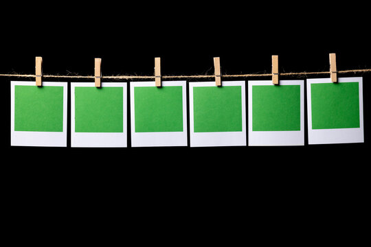 Six green rectangular sheets of paper in a white frame hang from a thin thread against a black background, attached with a clothespin, side view. Space for text.