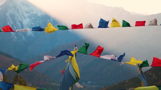 Landscape shot of colorful Buddhist prayer flags waving in front of snowy Himalayan mountain peak during the sunset as seen from Tayul Monastery near Keylong in Lahaul Valley, Himachal Pradesh, India.