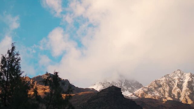 Landscape shot of orange clouds above the snow covered Himalayan mountain peaks during the sunset as seen from Keylong in Himachal Pradesh, India. Sunset above Himalayas in spring season.