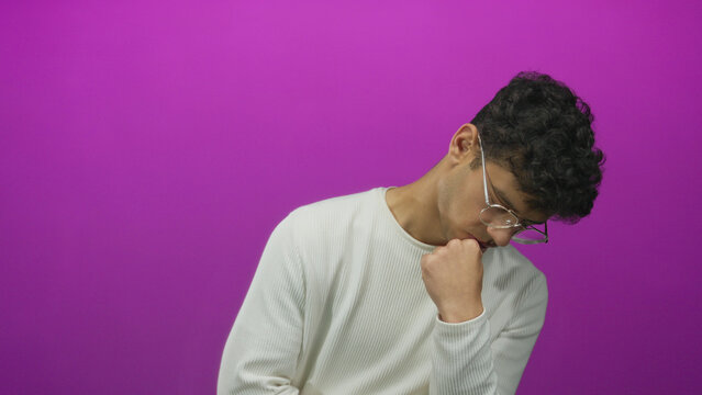 Young hispanic man wearing glasses holds his chin with his hand in studio scene; pensive reflection.