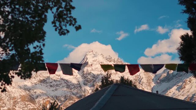 Defocused prayer flags waving in front of snow covered Himalayan mountain peak during the sunset as seen from Keylong in Lahaul and Spiti district, Himachal Pradesh, India. Scenic Natural background.