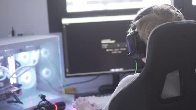 A teenage boy sits at a computer in a modern home setup, learning programming and typing code while focused on developing digital skills