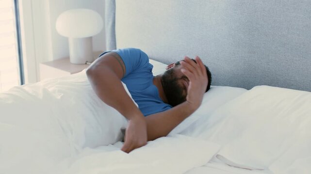 A man with dark skin is sleeping in a cozy bed. The room is bright and well-lit, creating a warm atmosphere. Soft bedding surrounds him as he rests peacefully during the day.