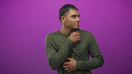 Obraz premium Man in green shirt holding his wrist and folding arms against a purple studio backdrop; quiet introspection calm.