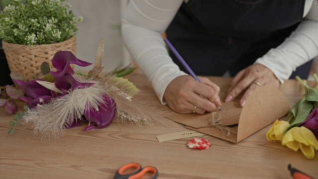 Woman florist writing with a purple pen and tying twine on a kraft envelope in a studio; care craft.
