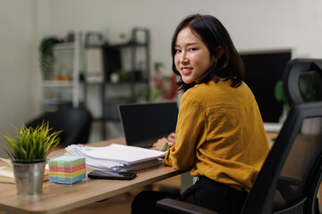 Obraz premium Young Asian woman smiling while working on a laptop
