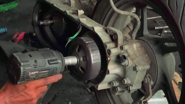 An industrial scene of a mechanic repairing a motorcycle engine with a power drill in a professional workshop setting.
