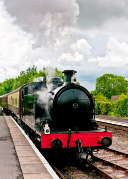 A steam train at a station, with steam billowing from the engine.