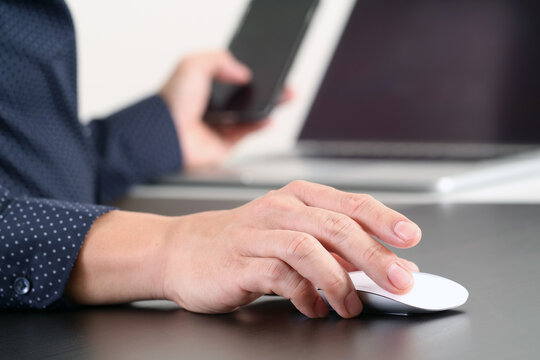 Businessman Using Computer Mouse While Holding Smartphone at Desk