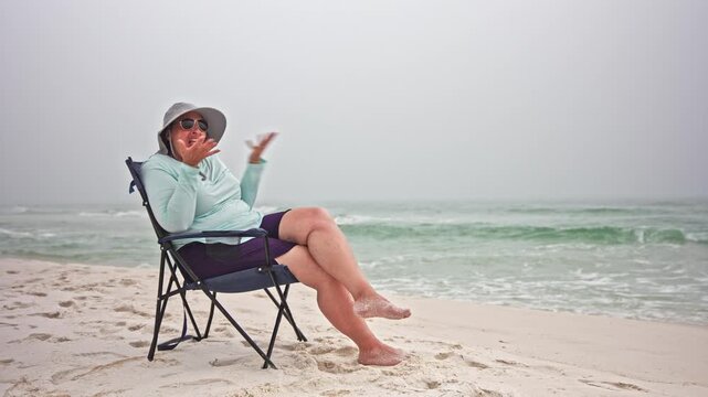 Plus size woman sits on a folding chair at the beach on a foggy day upset with person off camera lighthearted