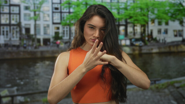 Young hispanic woman slams fist against palm on street by river canal lined with buildings; anger frustration.
