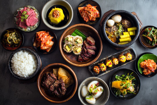 A colorful food photography spread of Korean national dishes including grilled meat, bibimbap, kimbap, tteokbokki, various sauces, and banchan like kimchi and jorim.