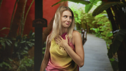 Obraz premium Woman hand on chest smiling on resort garden path beside tropical foliage and wooden boardwalk; gratitude calm.