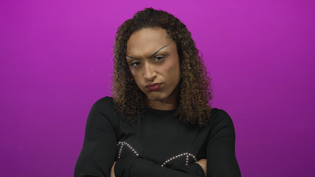 Woman with curly hair, wearing hoop earrings, arms crossed and pouting lips in a purple studio portrait session; rejection defiance.