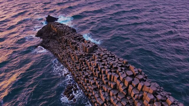 Aerial view of stunning rock formation on coastline. Waves crash against hexagonal stones during sunset. Scenic beauty creates tranquil atmosphere for nature lovers.