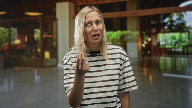 Woman with hand on forehead and pinched fingers making facepalm and dismissive gestures inside building lobby reception; frustration waiting.