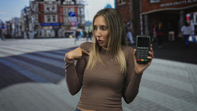 Woman points finger to card reader while holding payment terminal on a busy city street near shops; payment confusion.