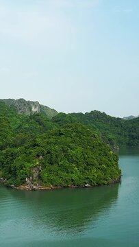 Scenic view of a green, forested island surrounded by calm turquoise waters in Ha Long Bay, Vietnam, under a clear blue sky.
