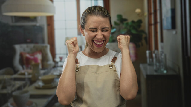 Woman with clasped bare hands and closed eyes in a building living room kitchen area by sofa and lamp facing camera; gratitude simplicity comfort warmth.
