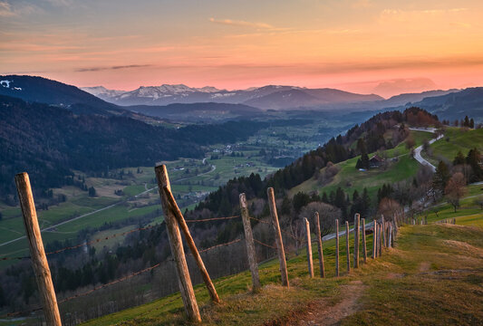  landscape in Bregenzer Wald at sunset with partly snow-covered mountains and Saentis summit glowing in warm evening light under a dramatic sky. Austria, Vorarlberg