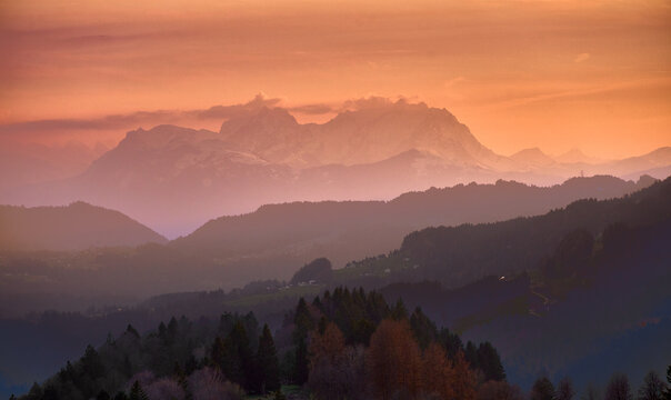  landscape in Bregenzer Wald at sunset with partly snow-covered mountains and Saentis summit glowing in warm evening light under a dramatic sky. Austria, Vorarlberg