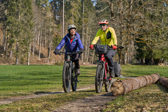 Happy senior couple enjoying an active lifestyle, riding electric bikes on a forest trail in spring. Outdoor recreation, healthy aging, and leisure time in nature on a sunny day.