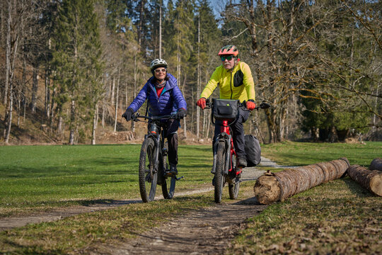 Happy senior couple enjoying an active lifestyle, riding electric bikes on a forest trail in spring. Outdoor recreation, healthy aging, and leisure time in nature on a sunny day.