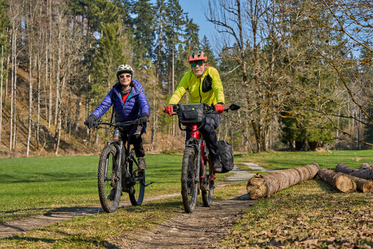 Happy senior couple enjoying an active lifestyle, riding electric bikes on a forest trail in spring. Outdoor recreation, healthy aging, and leisure time in nature on a sunny day.