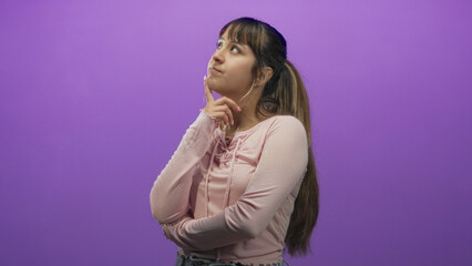 Fototapeta premium Woman with hand on chin and squinting gaze, crossed arms and casual pink shirt in studio; pensive reflection.