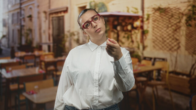 Woman pointing finger at camera in street cafe dining area, wearing white shirt and red glasses; accusation accountability.
