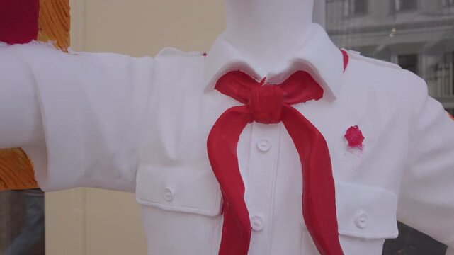 White statue of a Soviet pioneer boy stands in a city environment. The young bugler wears a red necktie and holds a trumpet with a small flag.