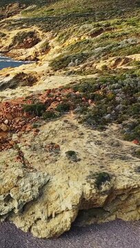 Scenic view of rugged rocky cliffs and clear blue sea along the Delta du Fango coastline in Corsica, France. Natural Mediterranean landscape with textured stone and coastal vegetation.