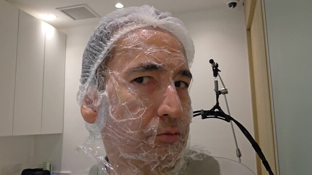 Treatment, cure of face skin in dermatology clinic. Acne Scars laser procedure for man. Man with cream with anesthesia and plastic film on his face before laser therapy procedure.