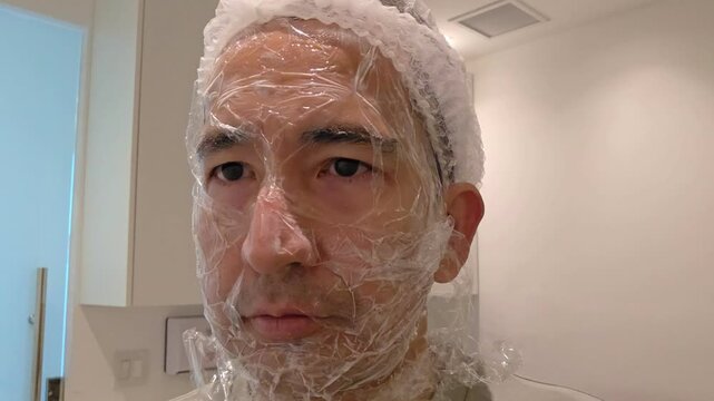 Treatment, cure of face skin in dermatology clinic. Acne Scars laser procedure for man. Man with cream with anesthesia and plastic film on his face before laser therapy procedure.